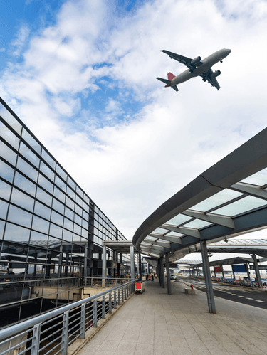 An airport departures area with an aeroplane visible overhead.
